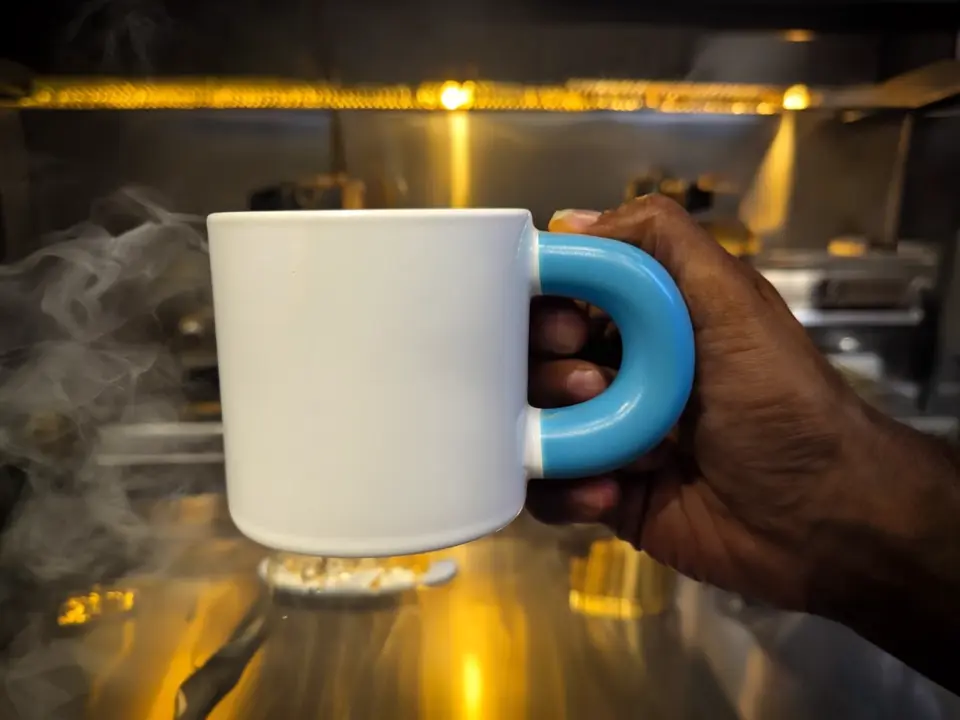 Cinematic product advertisement showing _mug_ being held by a right hand in a natural position in an elegant, modern kitchen setting. Low-key, moody lighting with warm tones and soft shadows creating a luxurious and d.webp